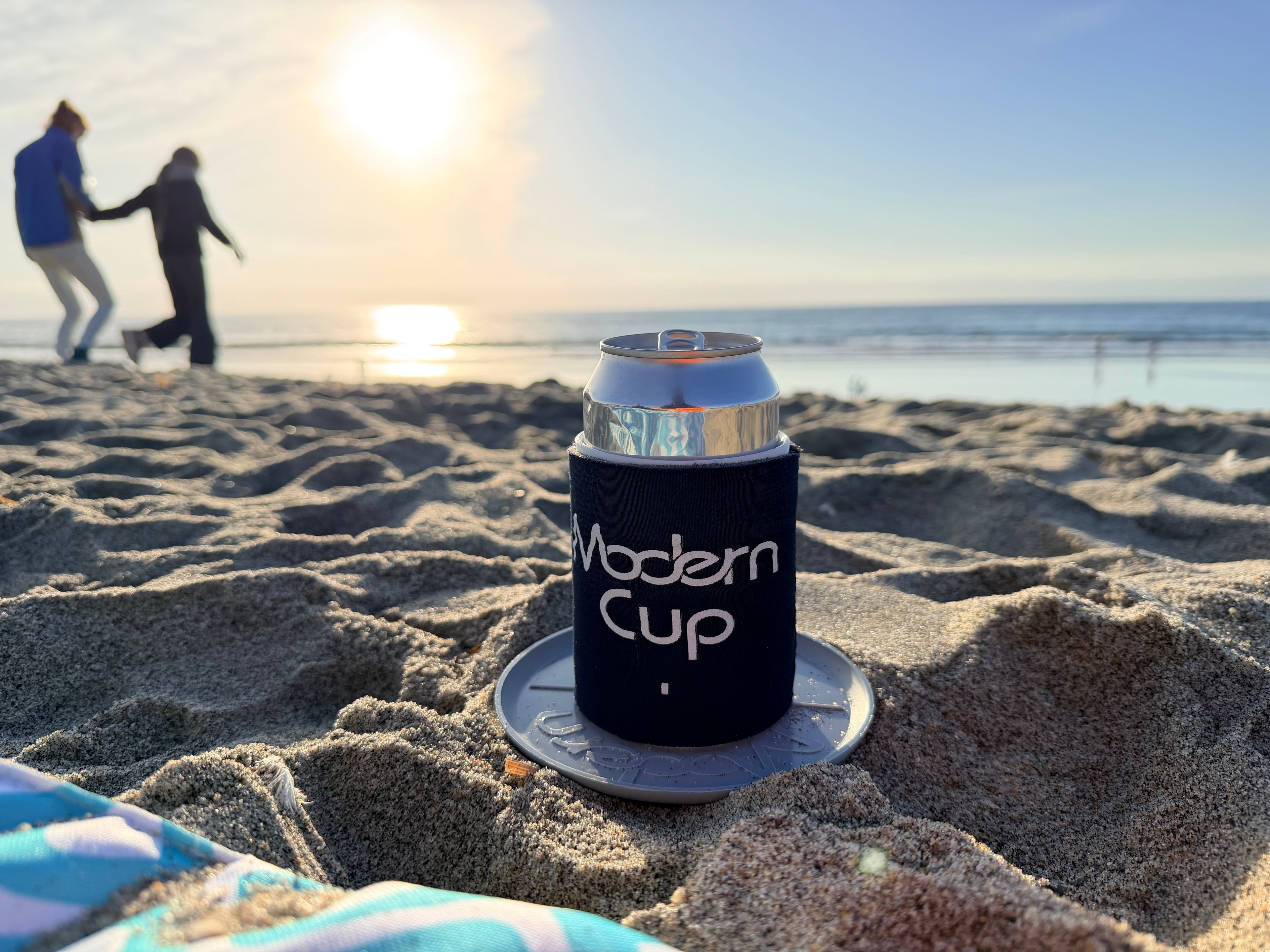 A beach scene at sunset with a can in a blue "Modern Cup"
